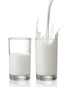 pouring milk creating splash with a glass of half full milk beside